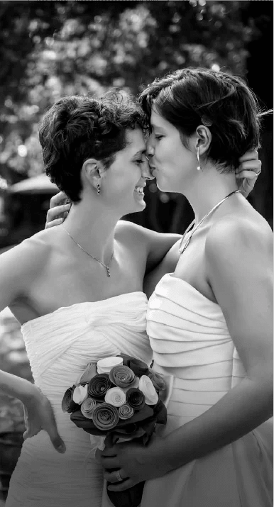 photo en noir et blanc - deux femmes en robes de mariées - l'une embrassant l'autre sur le front