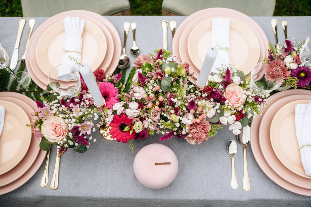 gros plan sur une table de mariage avex vaisselle rose et chamin de table constitué de multiples fleurs