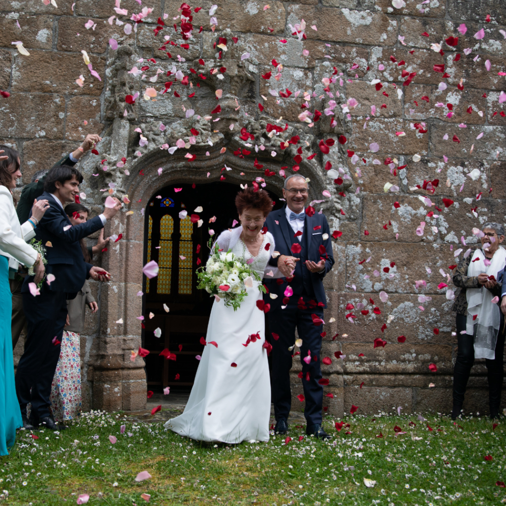 mariés sorttant de l'église sous une pluie de pétales de roses rouges