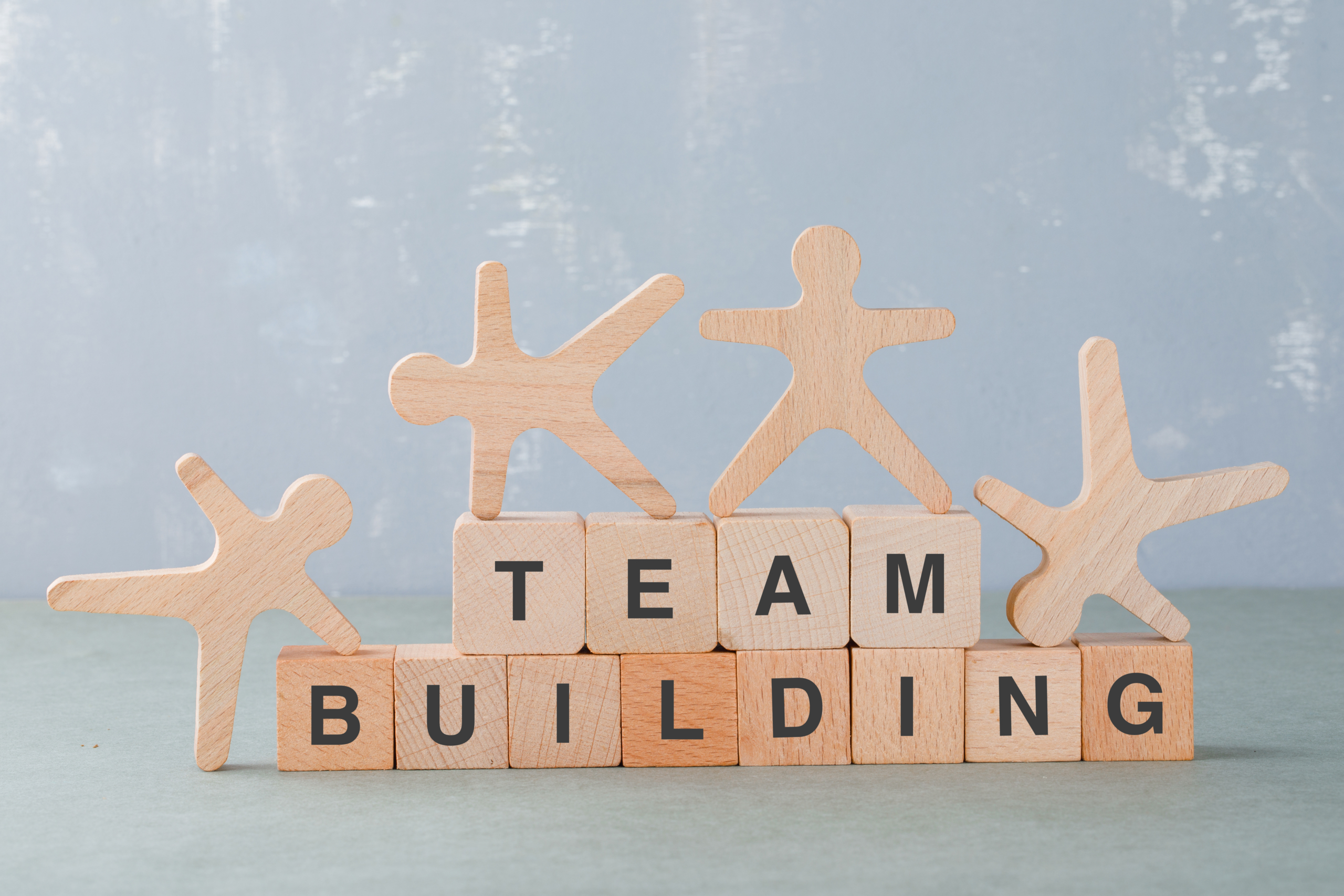 cube de bois formant les mots team building sur lesquels sont posés quatre bonhommes en bois