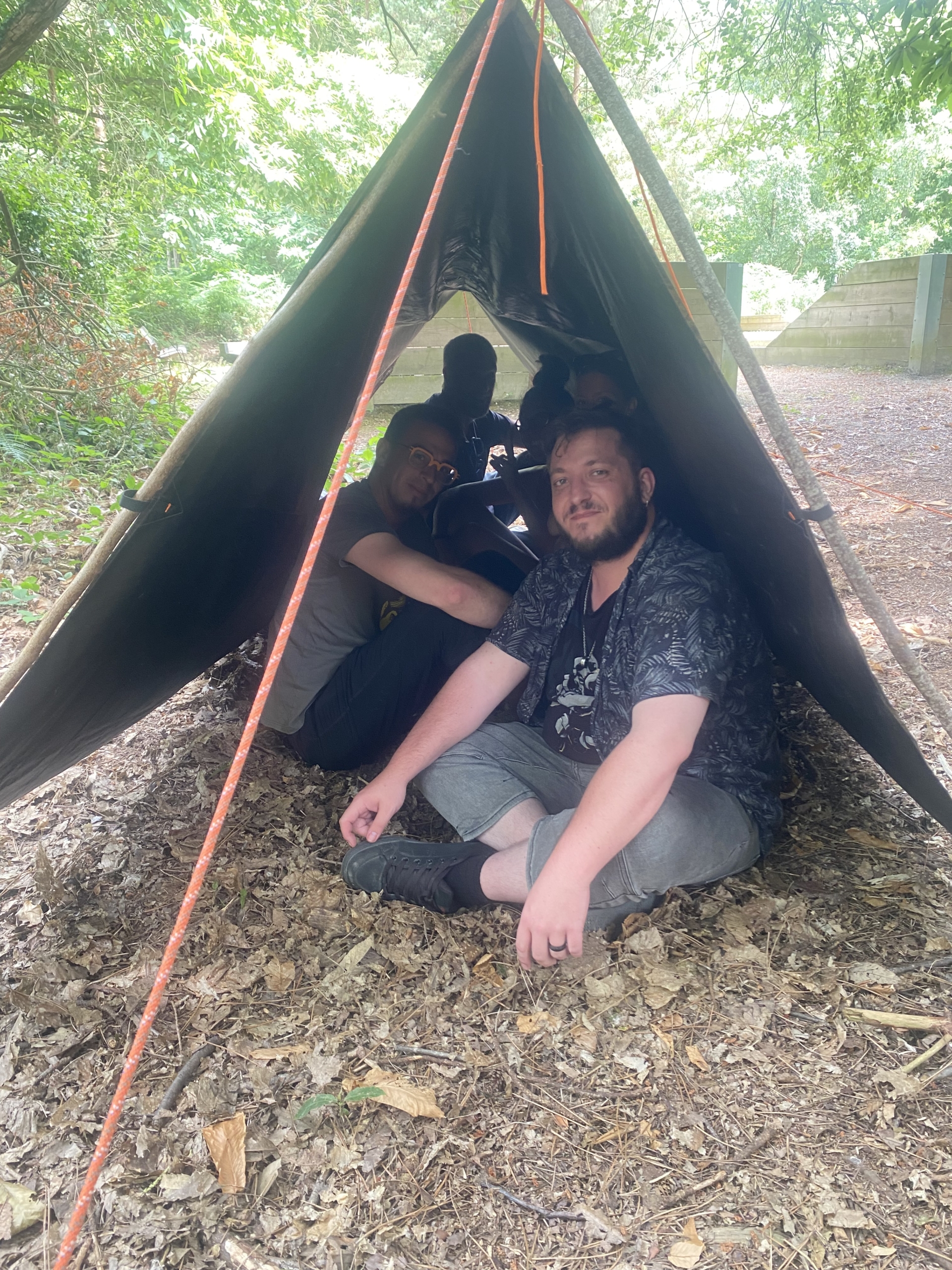 groupe de personnes assises sous une tente de fortune montée lors d'un team building olympiade survie en pleine nature par Glad events