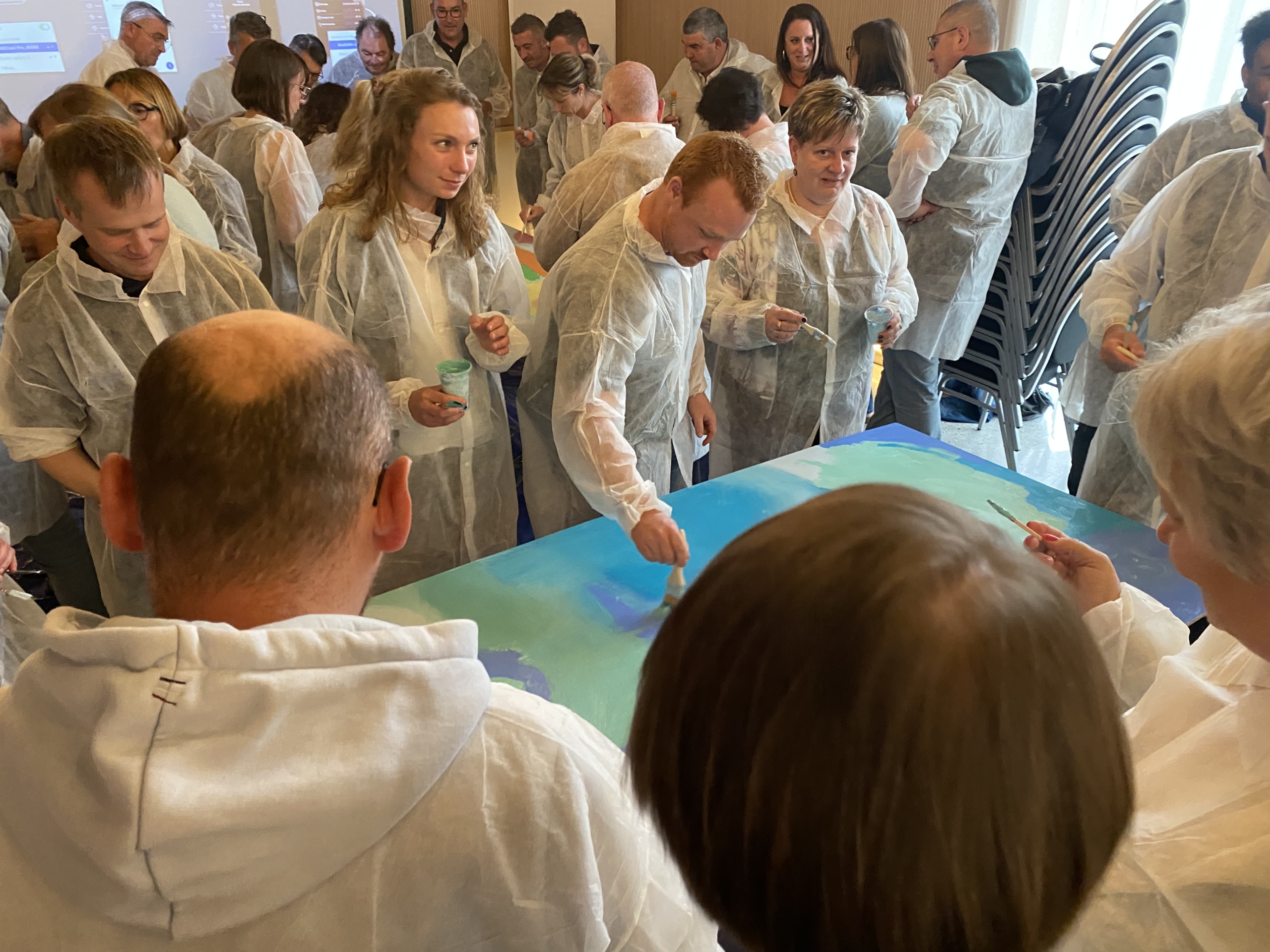 Atelier cohésion d'équipe peinture collective à Lorient par Glad events - grand groupe de collègues répartis autour de panneaux géants en train d'appliquer de la peinture dans des dégradés de bleu