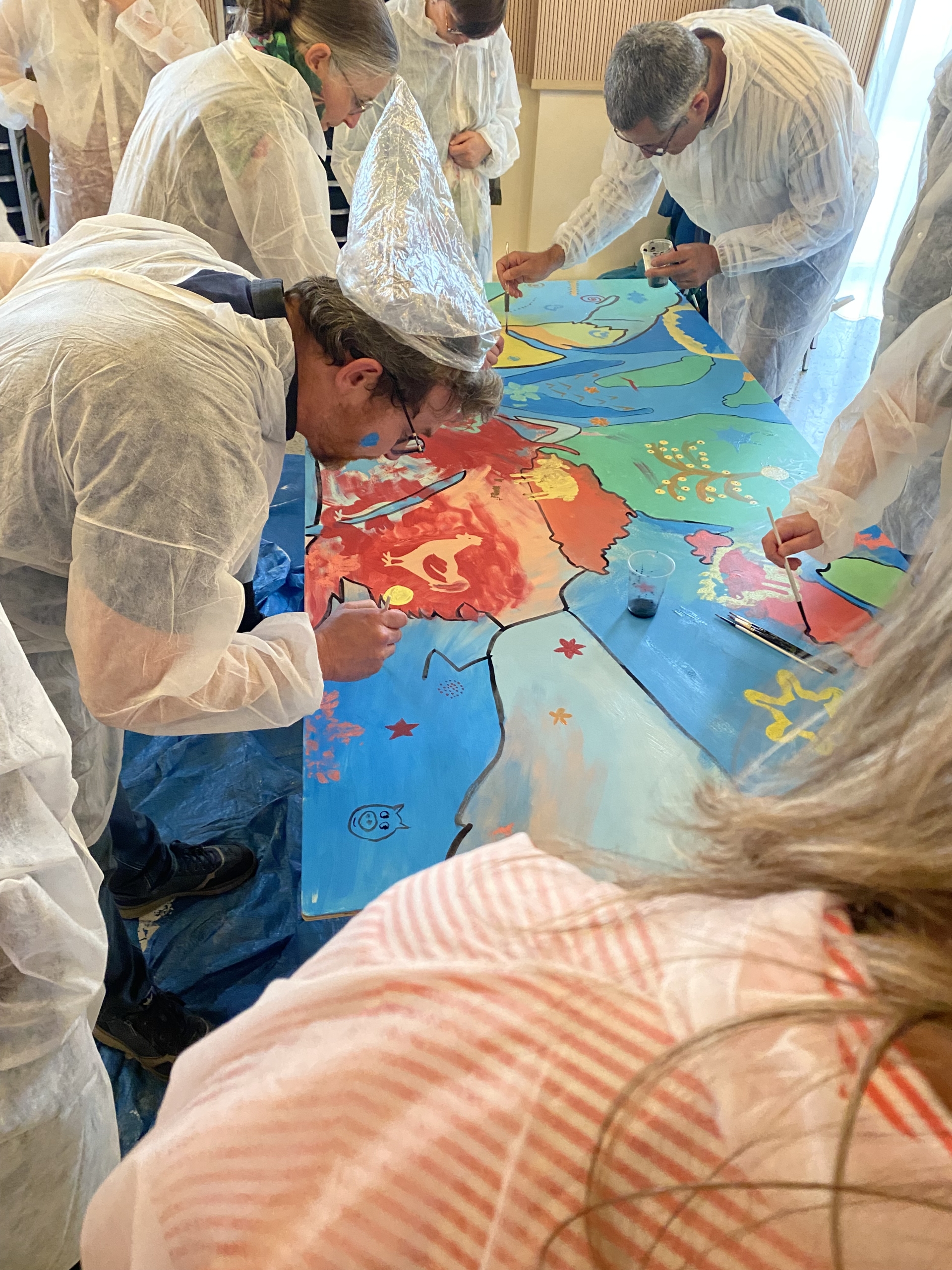 peinture collective Groupe autour d'une oeuvre collective en train de peindre lors d'un team building peinture collective par Glad events, agence évènementielle à St Malo