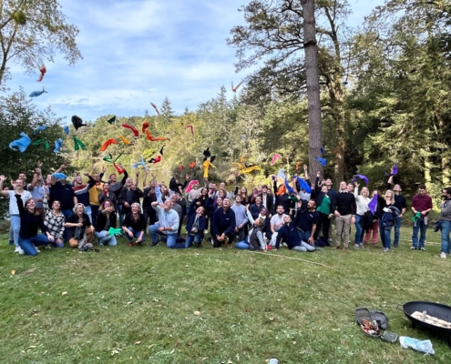 Groupe rassemblé sous les arbres lors d'un team building Glad events en Bretagne. Certains lancent leur fanions de couleurs différentes qui symbolisaient l'équipe à laquelle ils appartenait durant le jeu. Tous sourient et sur heureux