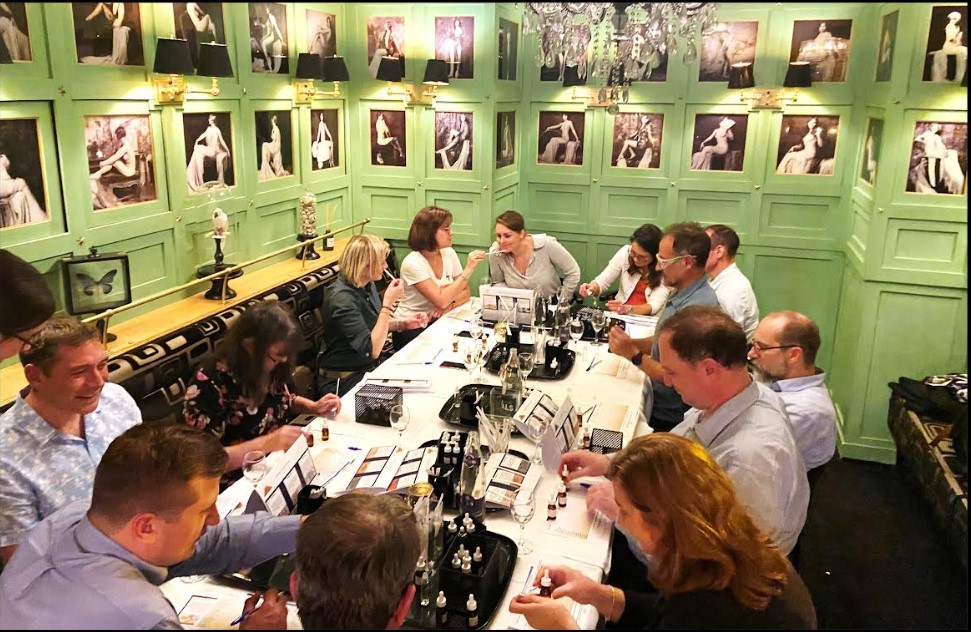 groupe de personnes assises autour d'une table dans une pièce verte pomme avec des cadres aux mur. Ils ont des éprouvettes, des fioles et des carnet de senteur devant eux lors du team building création de parfum par Glad events à Brest