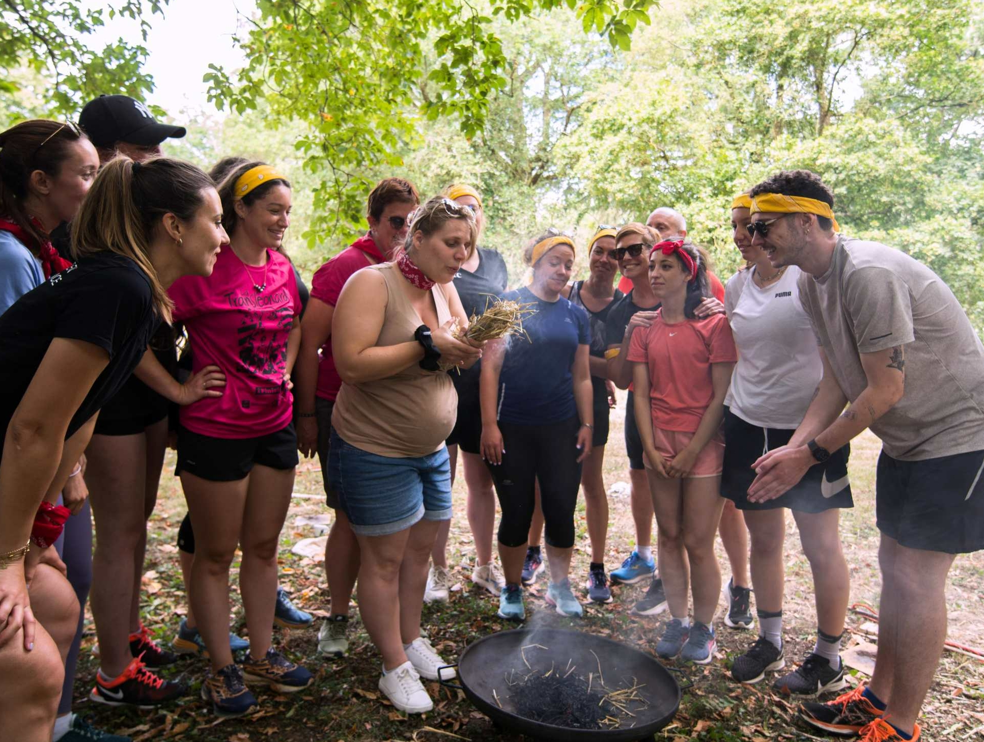 team building olympiades des défis 4 Glad events pro groupe de personnes souriantes autour d'une femme enceinte qui souffle sur de la paille pour allumer un feu lors d'un team building en Bretagne par Glad events